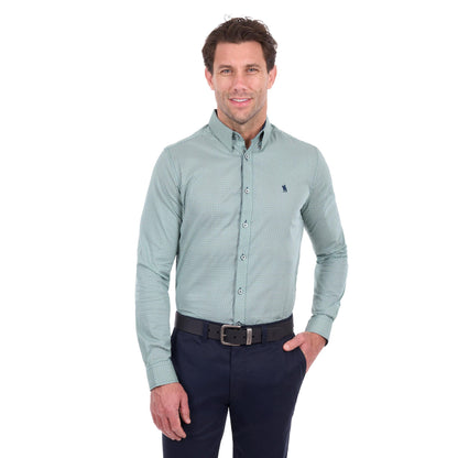 A man wearing a light sage green long-sleeve button-down shirt with a small micro-pattern, paired with dark navy trousers and a black belt, photographed against a solid white background.
