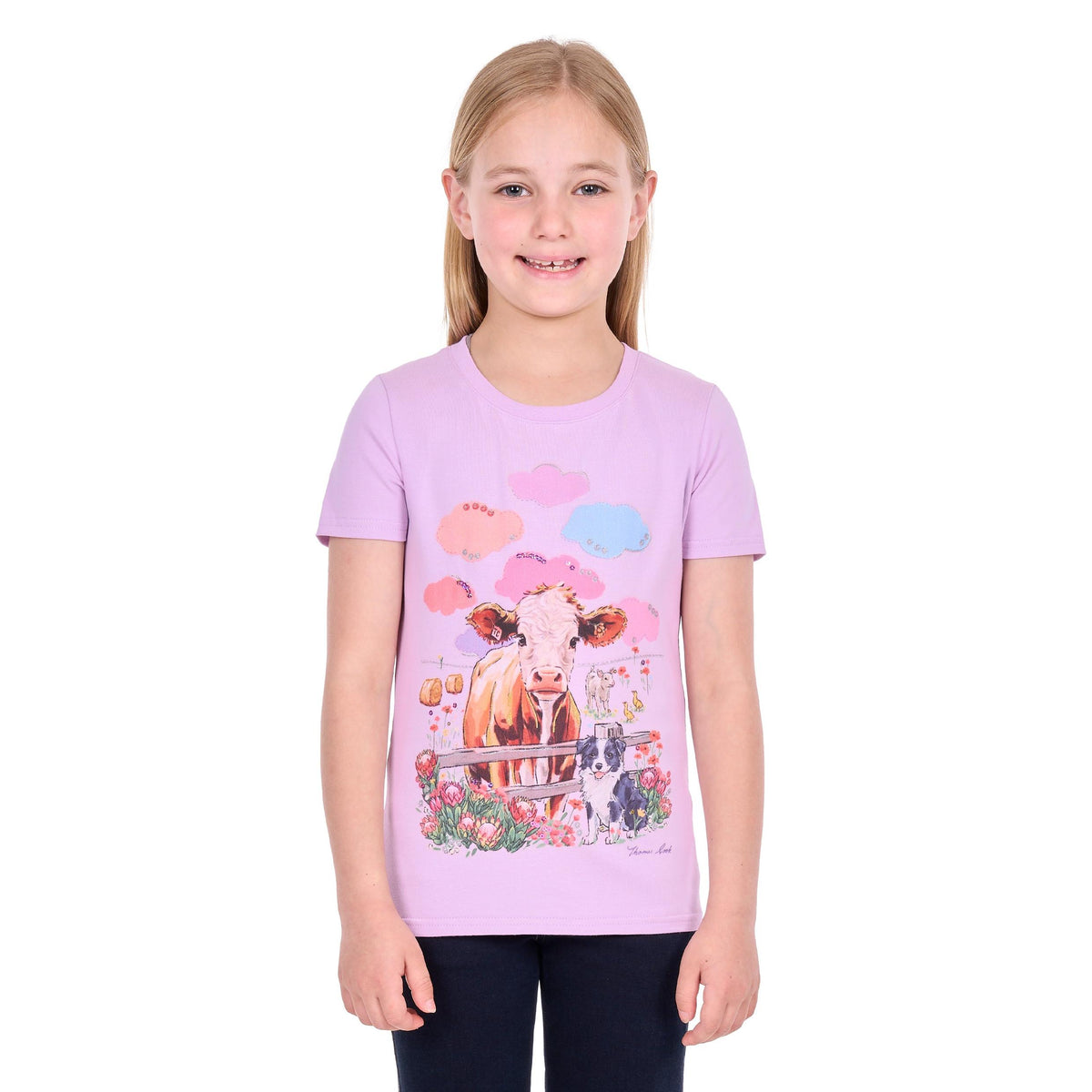A young girl with blonde hair wearing a light purple short-sleeve t-shirt with a colorful graphic of a cow, flowers, and clouds, paired with dark pants, against a plain white background.
