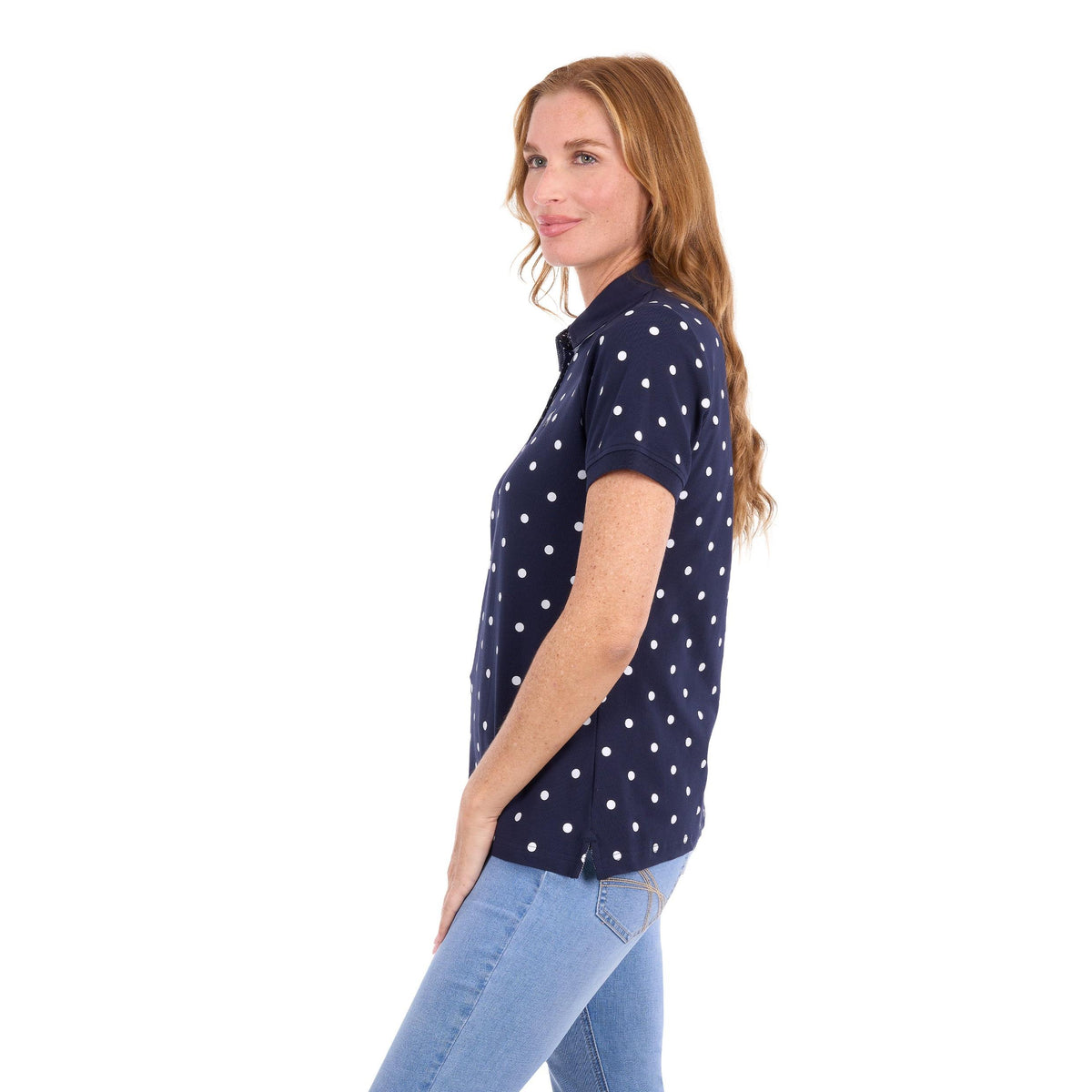 A woman with long light brown hair is shown in profile wearing a navy blue short-sleeve polo shirt with white polka dots, paired with light blue jeans, against a plain white background.