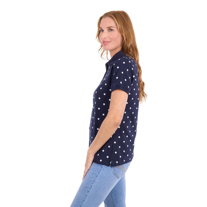 A woman with long light brown hair is shown in profile wearing a navy blue short-sleeve polo shirt with white polka dots, paired with light blue jeans, against a plain white background.