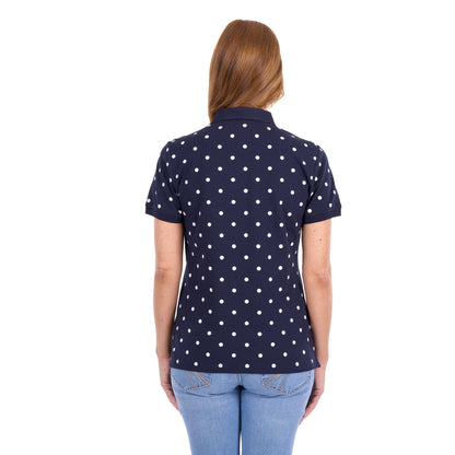 A woman viewed from the back wearing a navy blue short-sleeve polo shirt with a white polka dot pattern, paired with light blue jeans, against a plain white background.