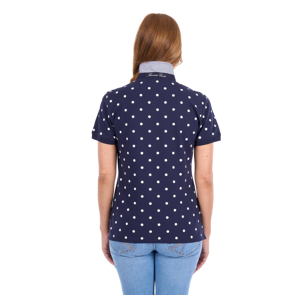A woman viewed from the back wearing a navy blue short-sleeve polo shirt with a white polka dot pattern and a light gray collar, paired with light blue jeans against a white background.
