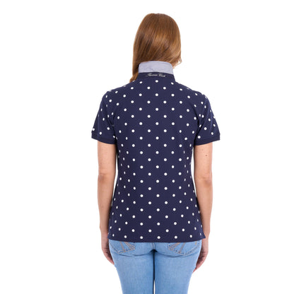 A woman viewed from the back wearing a navy blue short-sleeve polo shirt with a white polka dot pattern and a light gray collar, paired with light blue jeans against a white background.