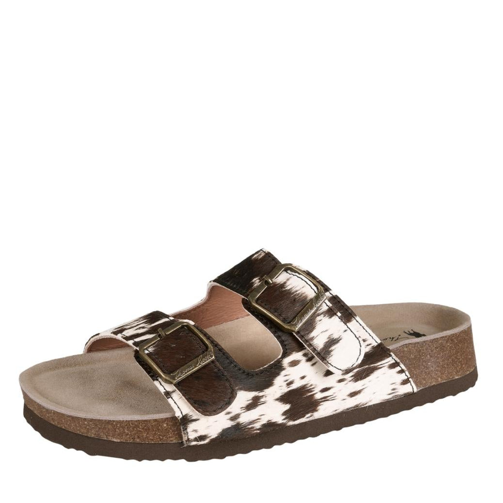 A single women's slide sandal with a brown and white cow-print upper strap, metallic gold buckle closures, and a brown cork-look midsole and outsole, shown against a plain white background.