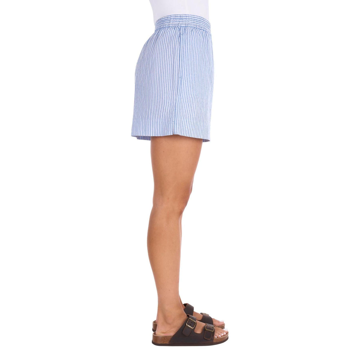 Side view of a person wearing light blue and white vertically striped shorts, paired with a white top and brown slide sandals, against a plain white background.